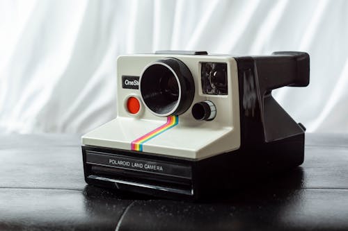 Vintage photo camera equipped with instant picture printer placed on leather surface against white curtain