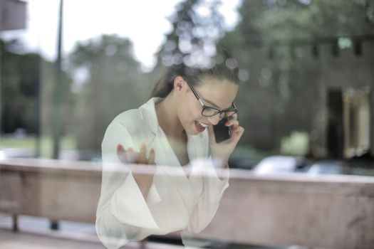 女商人戴着眼镜打电话，透过窗户向外看