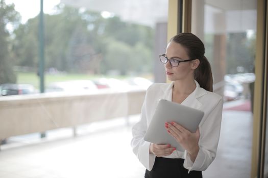 Businesswoman in office holding a tablet, looking thoughtfully out the window.