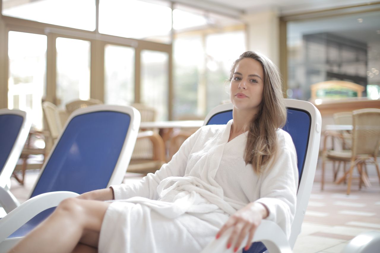 positive woman wearing bathrobe smiling and looking at camera while si