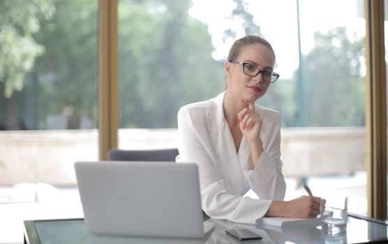 Confident woman in glasses working at a desk, embodying modern professionalism.