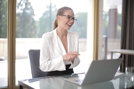 Confident businesswoman wearing glasses, working on laptop in bright modern office.
