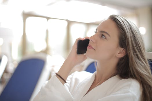 A woman in a white robe having a phone conversation in a cozy indoor setting.