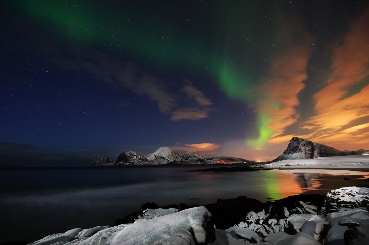 capture of the aurora borealis dancing over snowy mountains and calm s