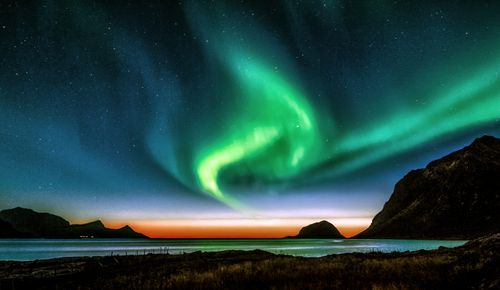 Free Stunning aurora borealis illuminates the night sky over Norway's scenic mountains and sea. Stock Photo
