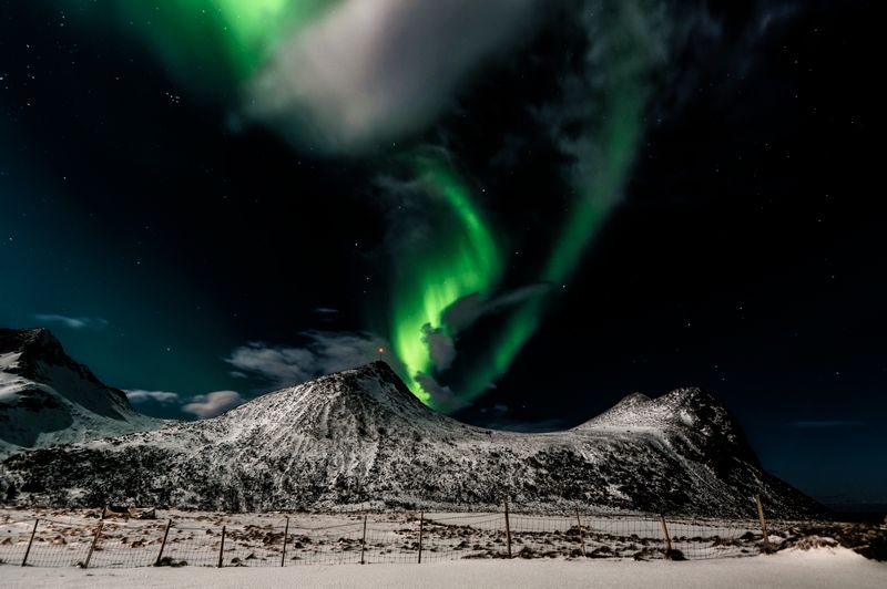 Aurora boreală deasupra unui munte acoperit cu zăpadă