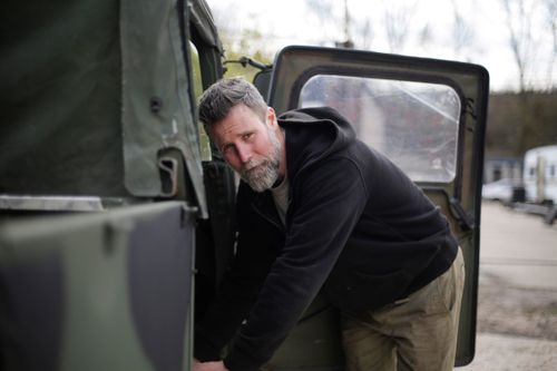 Free Side view of adult bearded man in workwear standing near door of car and checking details while working outside garage and looking at camera Stock Photo