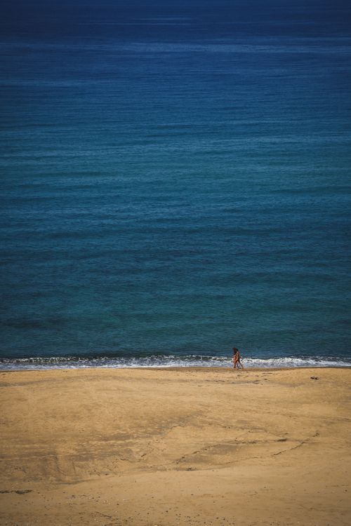 Free A lone person walks along a serene Sardinian beach by the blue sea. Stock Photo