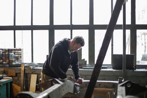 Adult bearded mechanic working with metal construction in garage