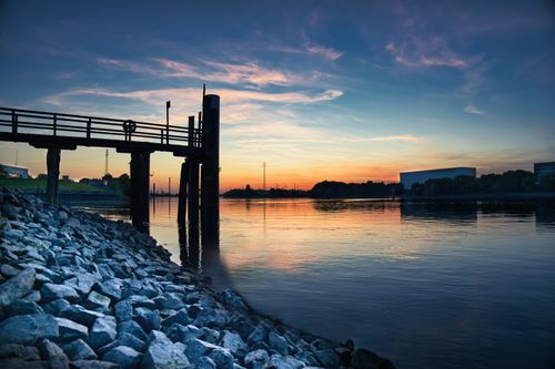 Free Calm river scene with a dock at sunset, featuring beautiful reflection and vibrant sky colors. Stock Photo