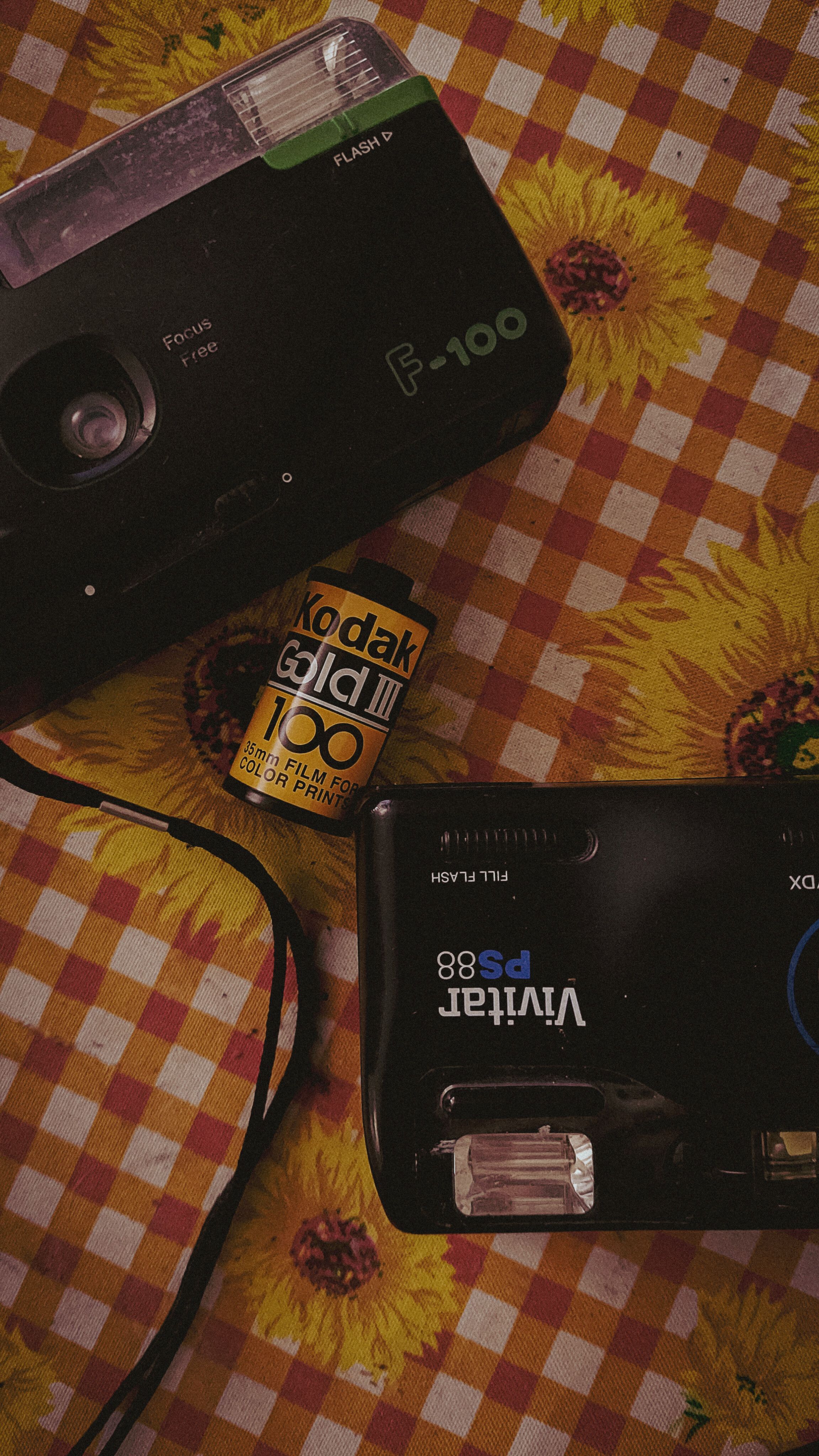 Retro film cameras with Kodak film roll on a sunflower-patterned tablecloth.