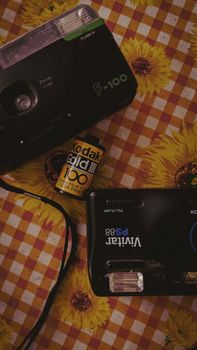 Retro film cameras with Kodak film roll on a sunflower-patterned tablecloth.