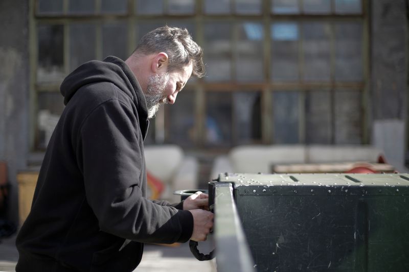 Side view of adult bearded mechanic in black workwear standing near car and fixing metal details while working on street near garage