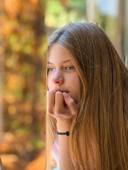 Free A young woman gazes thoughtfully outside, framed by autumn colors. Stock Photo