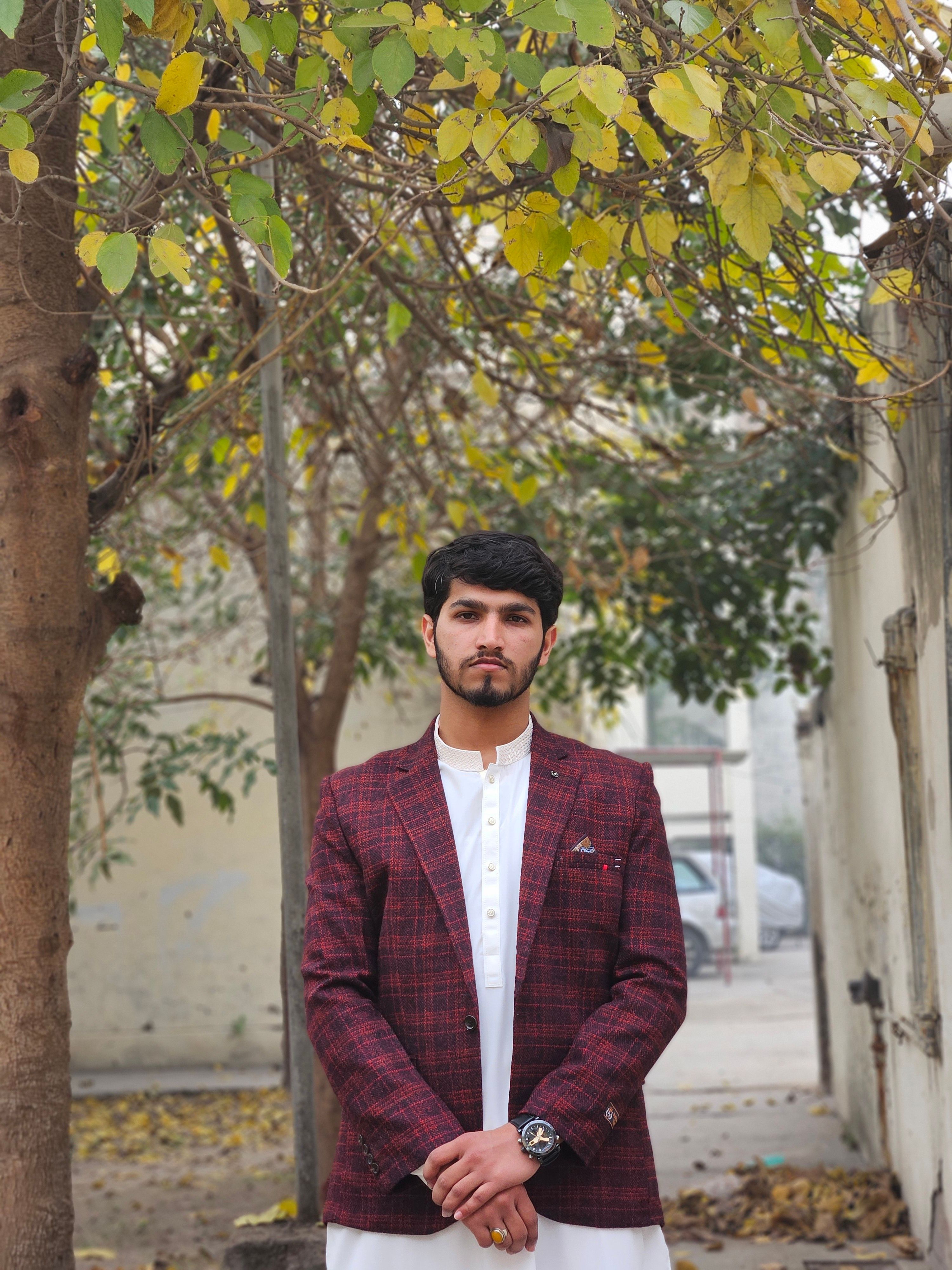 Portrait of a young man in a red plaid jacket standing outdoors in autumn.