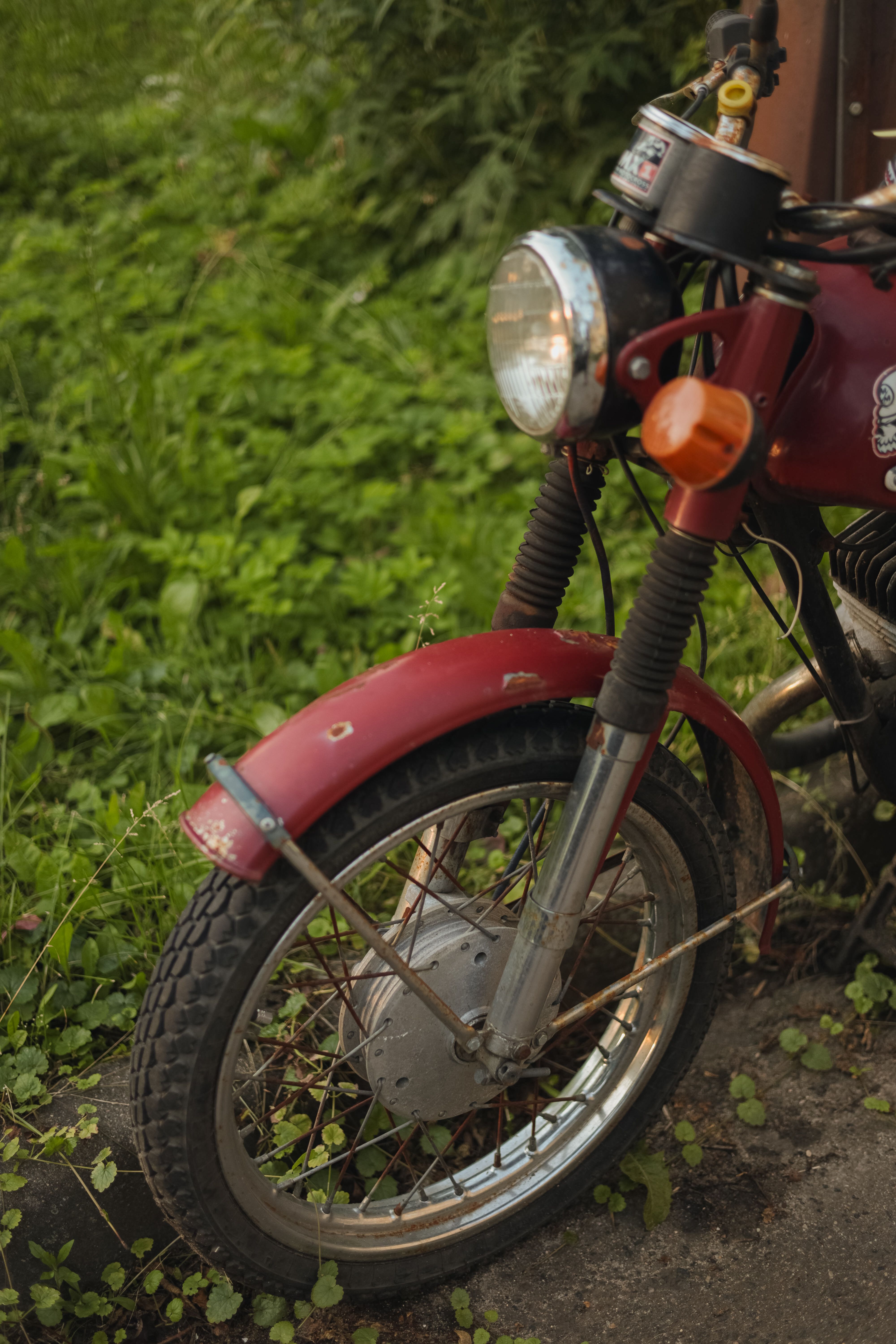 Close-up of a vintage red motorcycle parked on a grass-covered street corner.