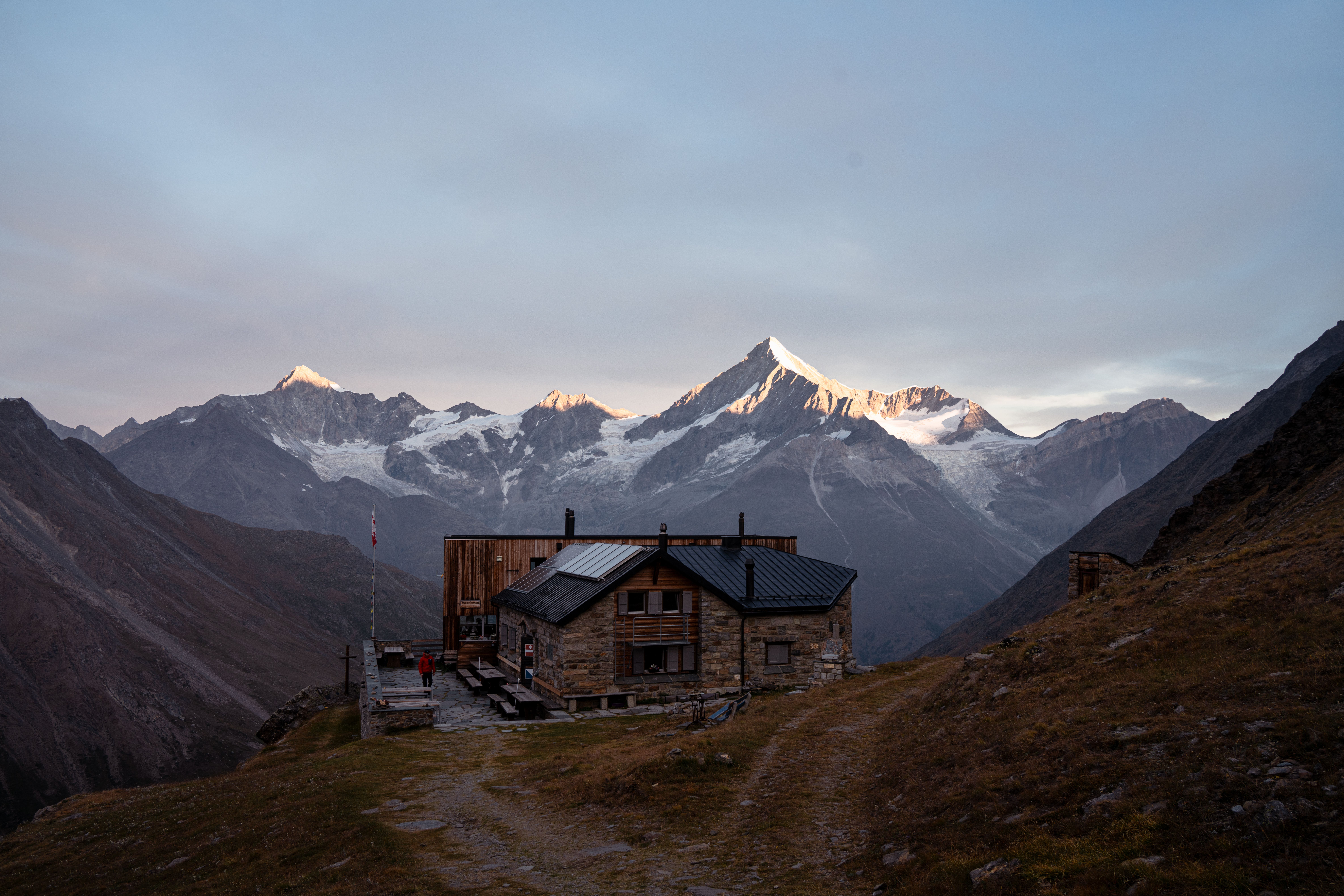 Un refuge de pierre et de bois au petit matin, face à une chaîne de sommets glaciaires.