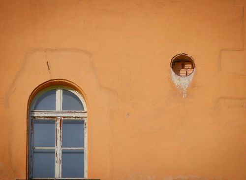 Free Rustic orange wall featuring a vintage wooden window and circular architectural detail. Stock Photo