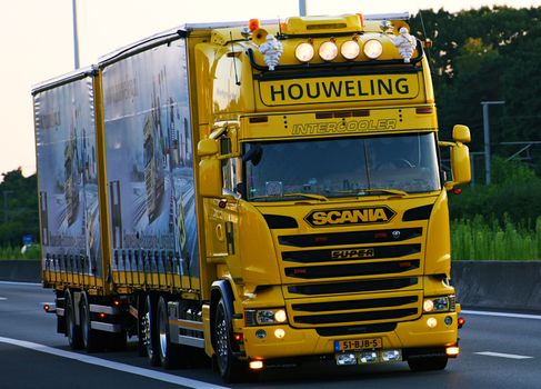 A vibrant yellow Scania truck with 'Houweling' branding driving on a highway.
