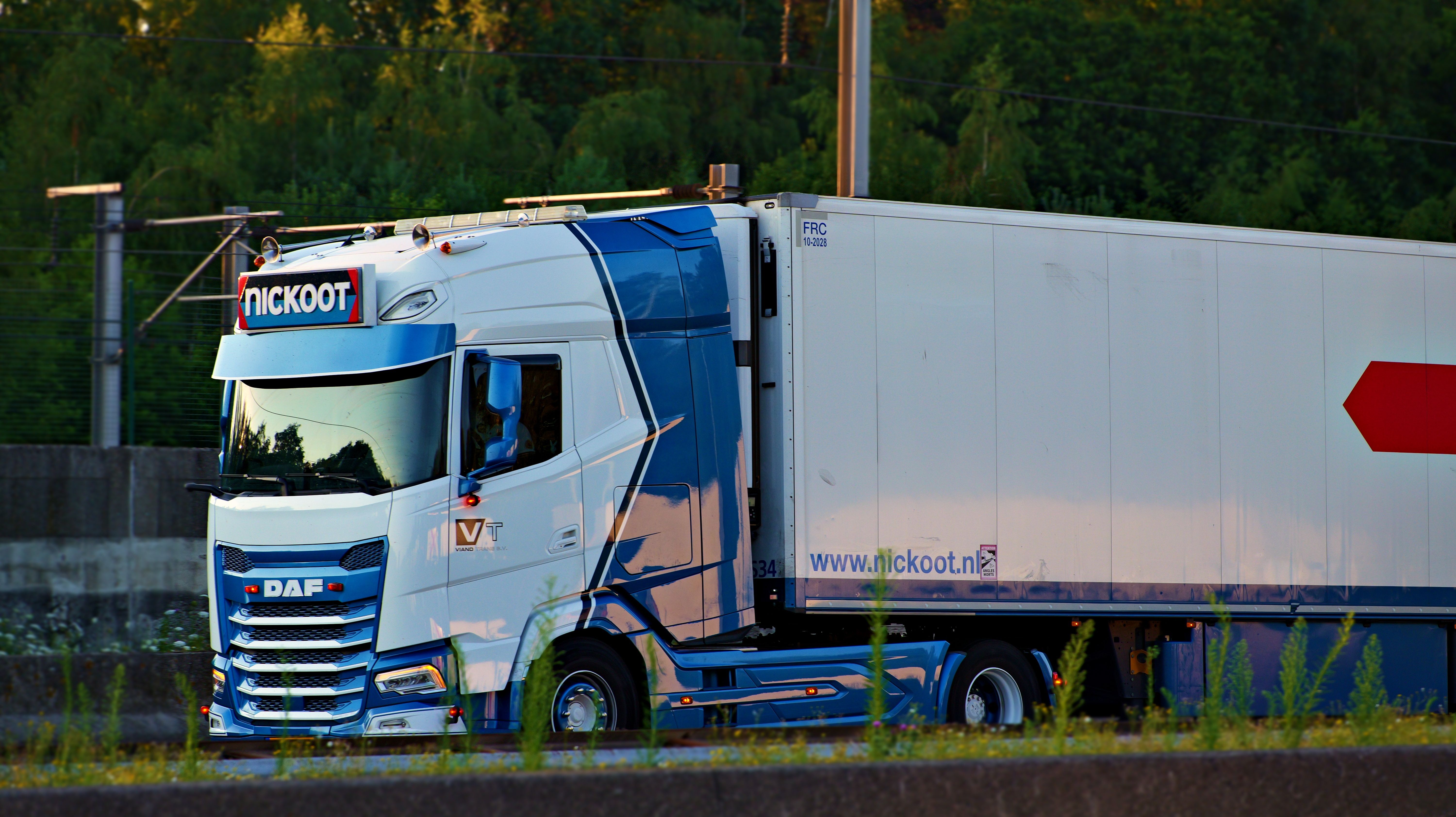 Blue DAF truck with a trailer driving on a highway in Antwerp, Belgium during sunset.