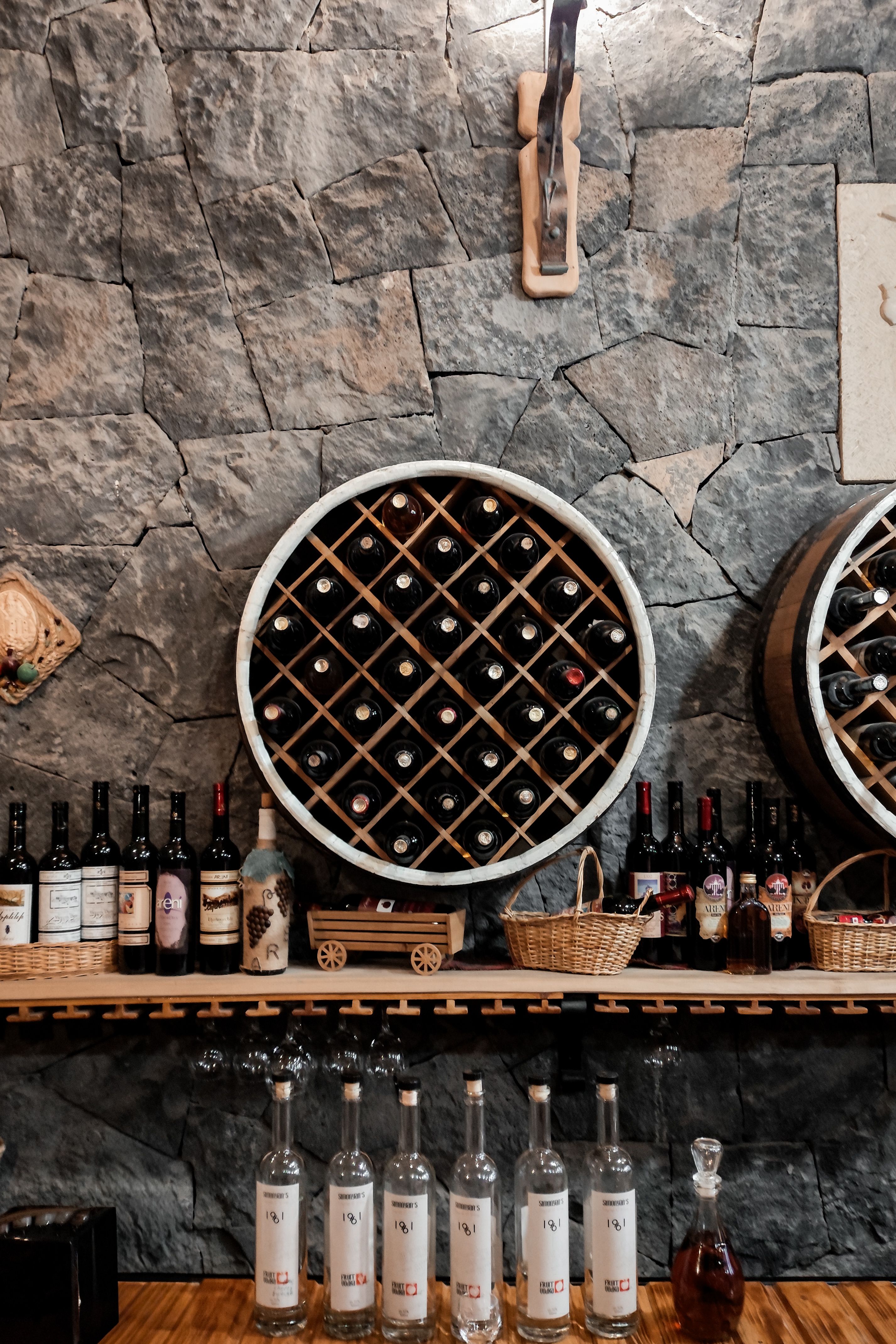 A rustic wine cellar scene featuring wine bottles on display against a stone wall in Areni, Armenia.