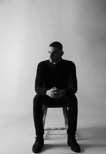 Monochrome portrait of a stylish man sitting with a serious expression.