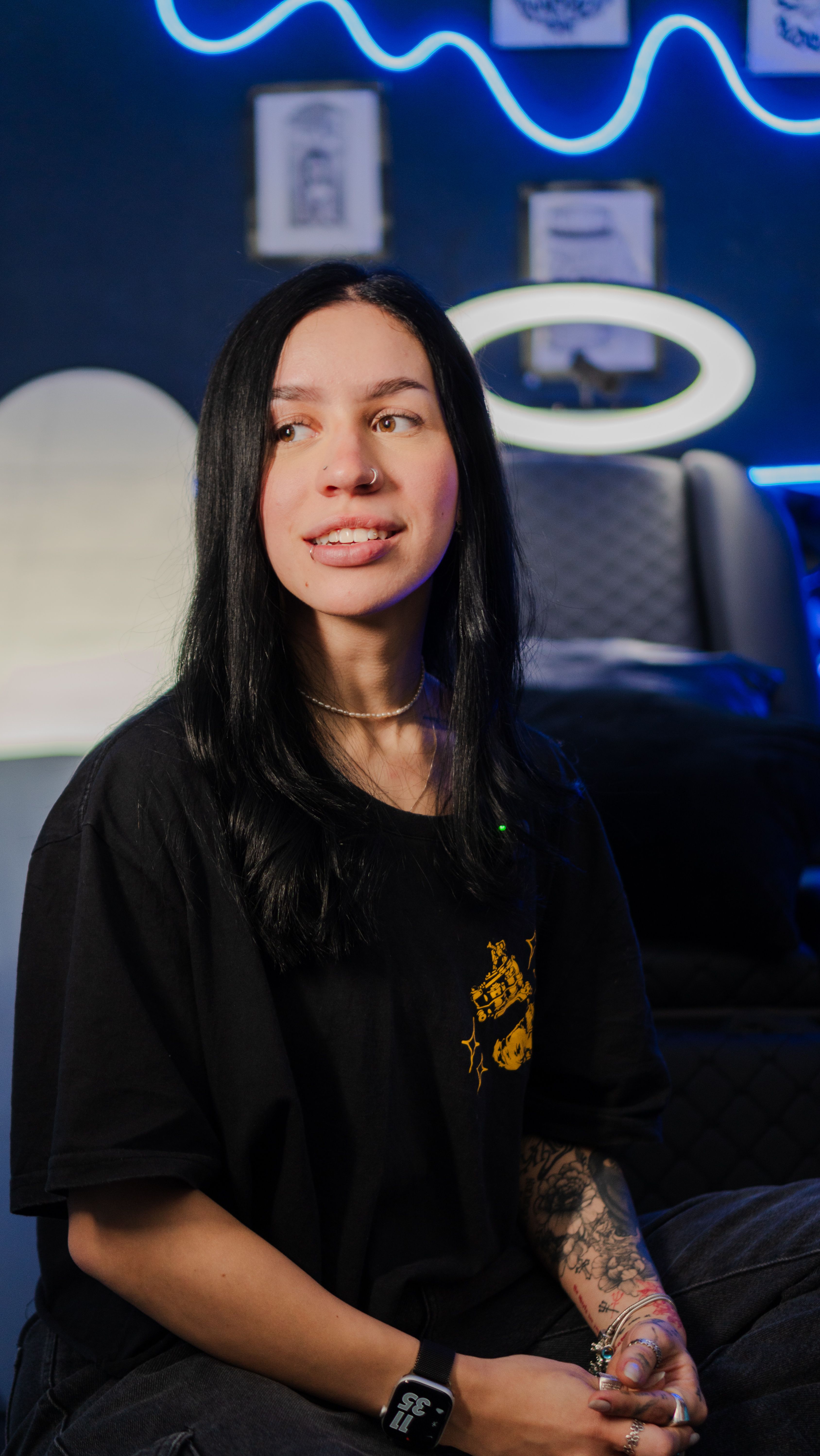 Young woman with tattoos in a modern room featuring neon lighting and artwork.