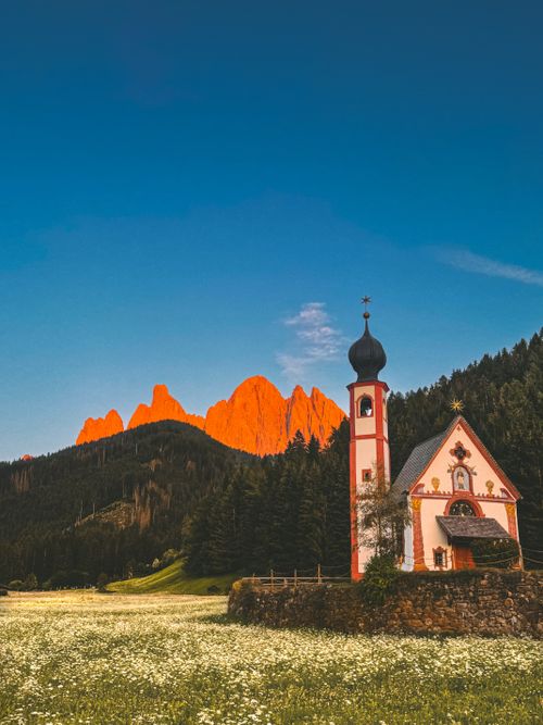 Free Picturesque chapel set against the dramatic backdrop of the sunlit Dolomites, evoking tranquility and beauty. Stock Photo
