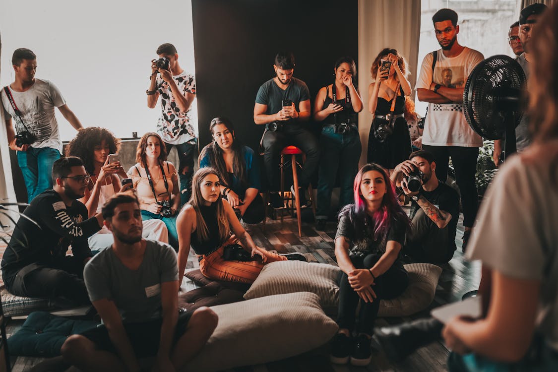 Group of multiethnic young people wearing casual clothes gathering together in spacious studio and listening attentively to female speaker