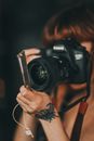 Crop unrecognizable female photographer with tattoo on hand taking pictures on professional photo camera against dark wall