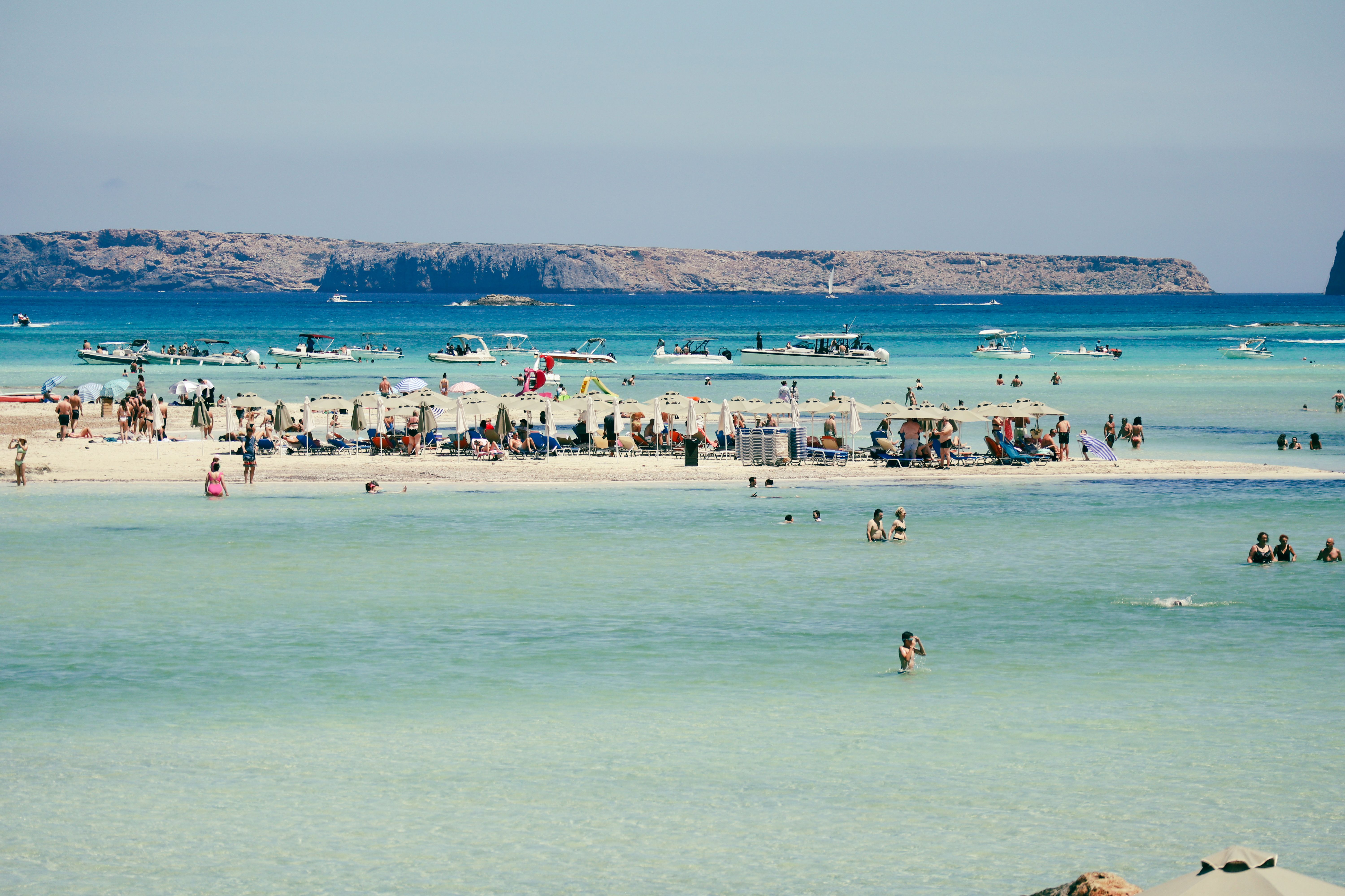 Vibrant beach scene with sunbathers and boats at a sunny seaside location.
