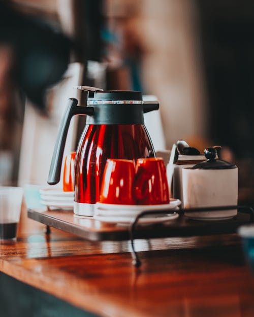 紅色陶瓷杯和水壺在咖啡廳的木製櫃檯上