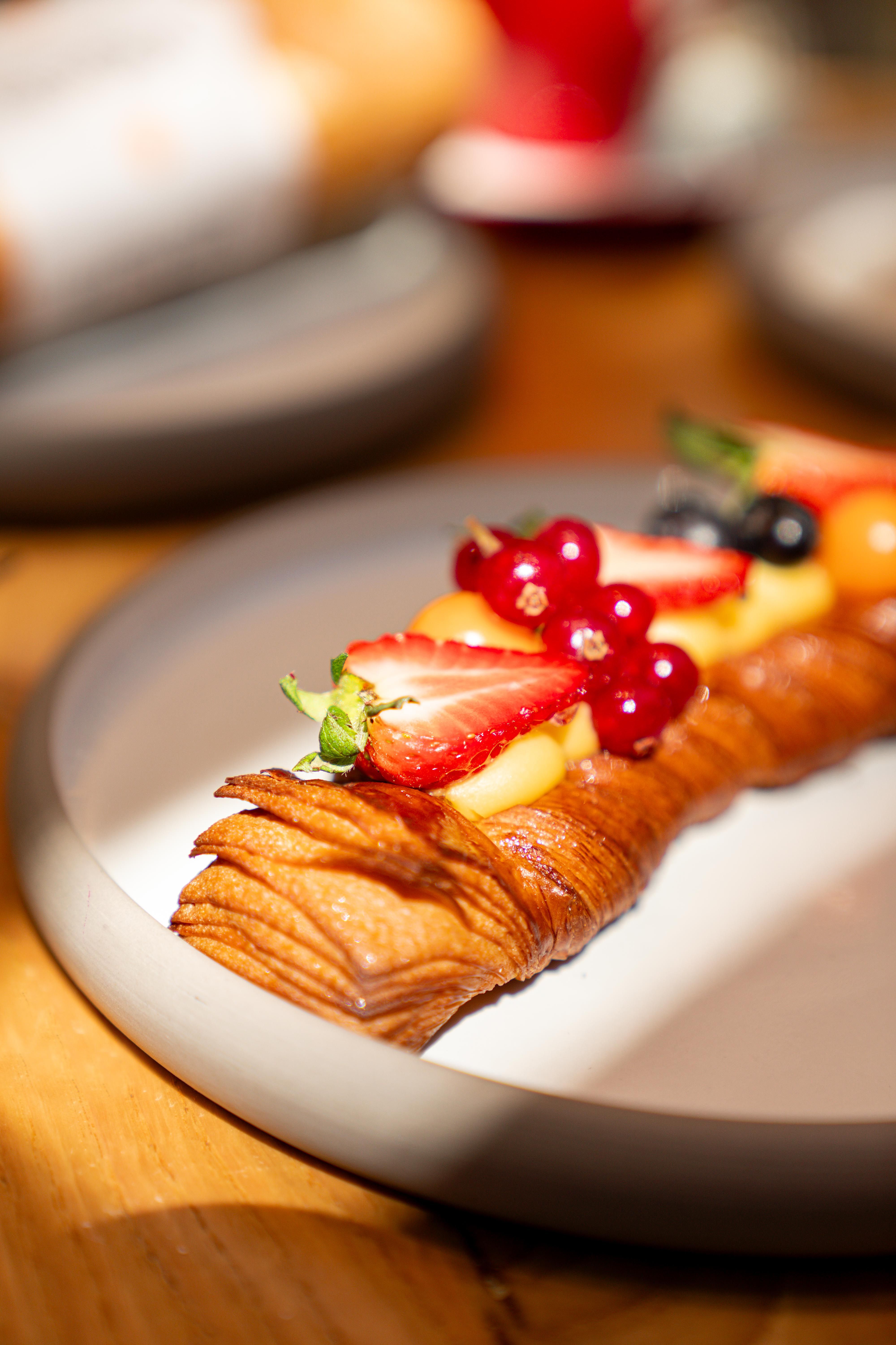 Close-up of a freshly baked pastry topped with strawberries, berries, and mint, served on a plate.