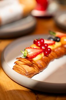 Close-up of a freshly baked pastry topped with strawberries, berries, and mint, served on a plate.