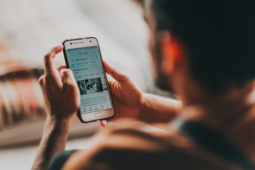 Free Back view of crop anonymous young male reading news on mobile phone while sitting in bedroom Stock Photo