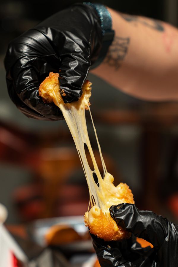 Arancini crocantes com queijo stretchy sendo despedaçado por uma mão com luva, mostrando comida reconfortante deliciosa.