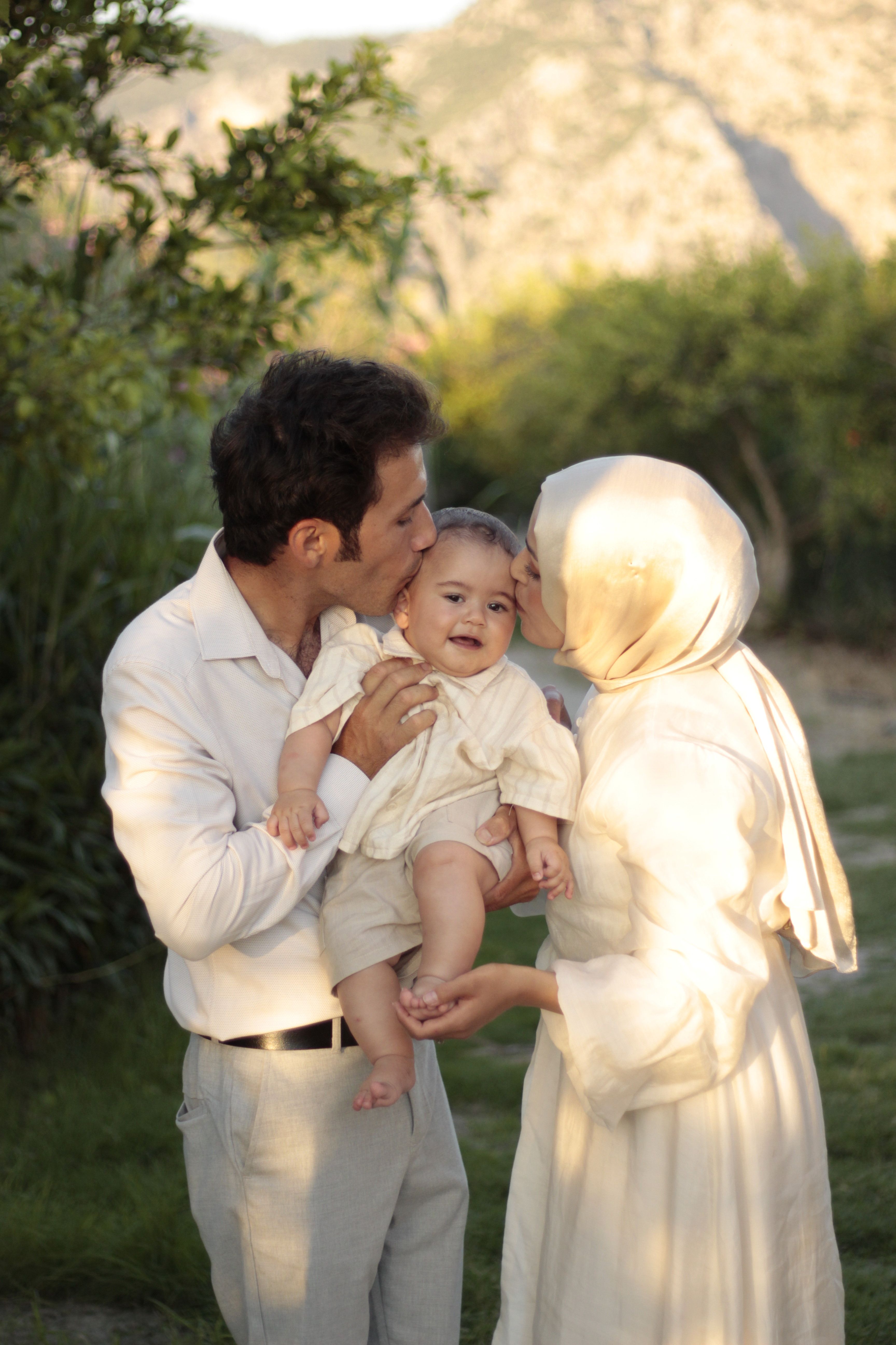 Loving parents kissing their baby in a sunny outdoor setting, capturing a warm family moment.