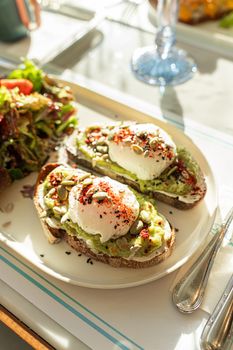 A beautifully plated avocado toast with poached eggs, garnished with seasoning and seeds, perfect for a healthy breakfast.