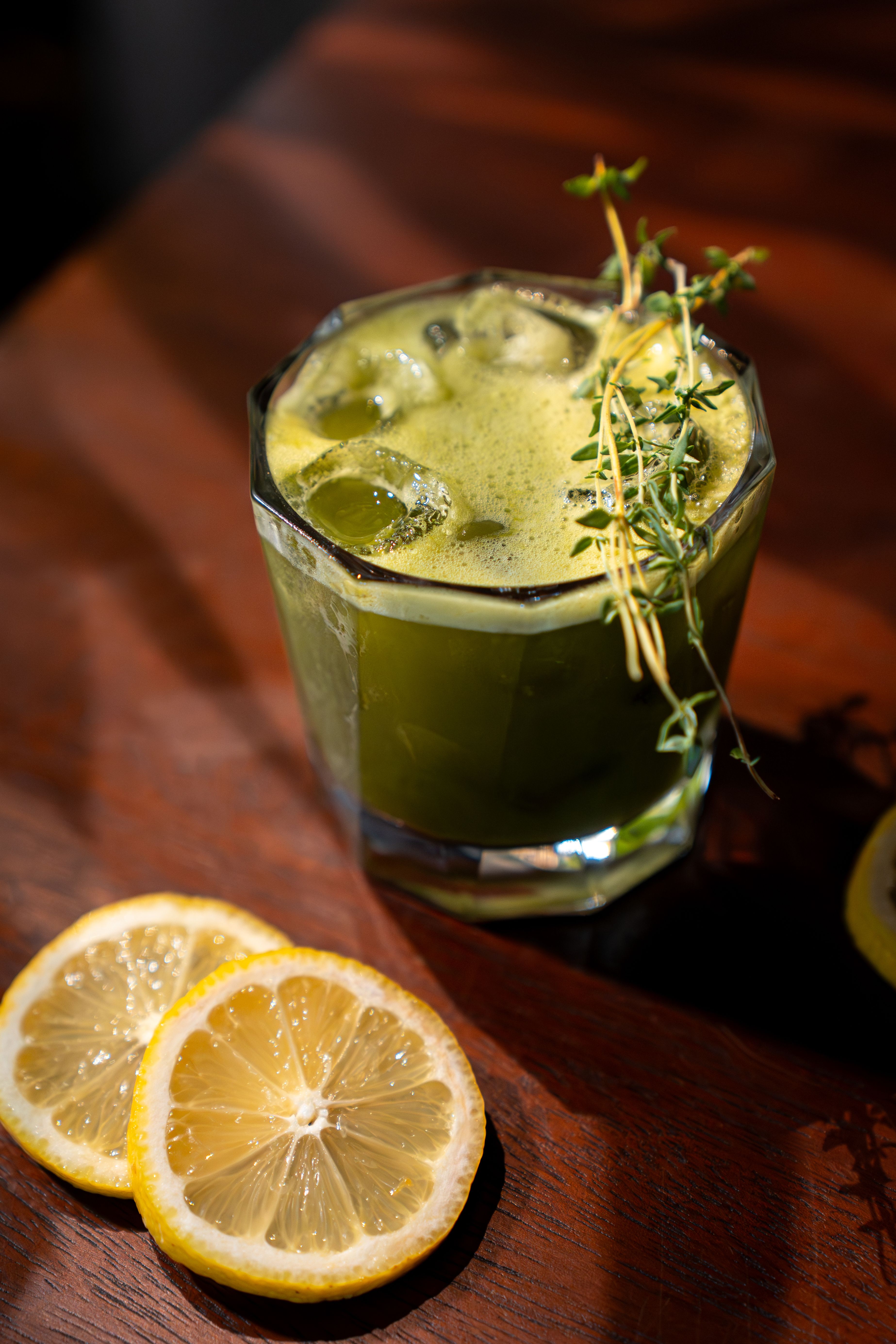 A fresh green juice drink with ice and thyme accentuated by lemon slices.