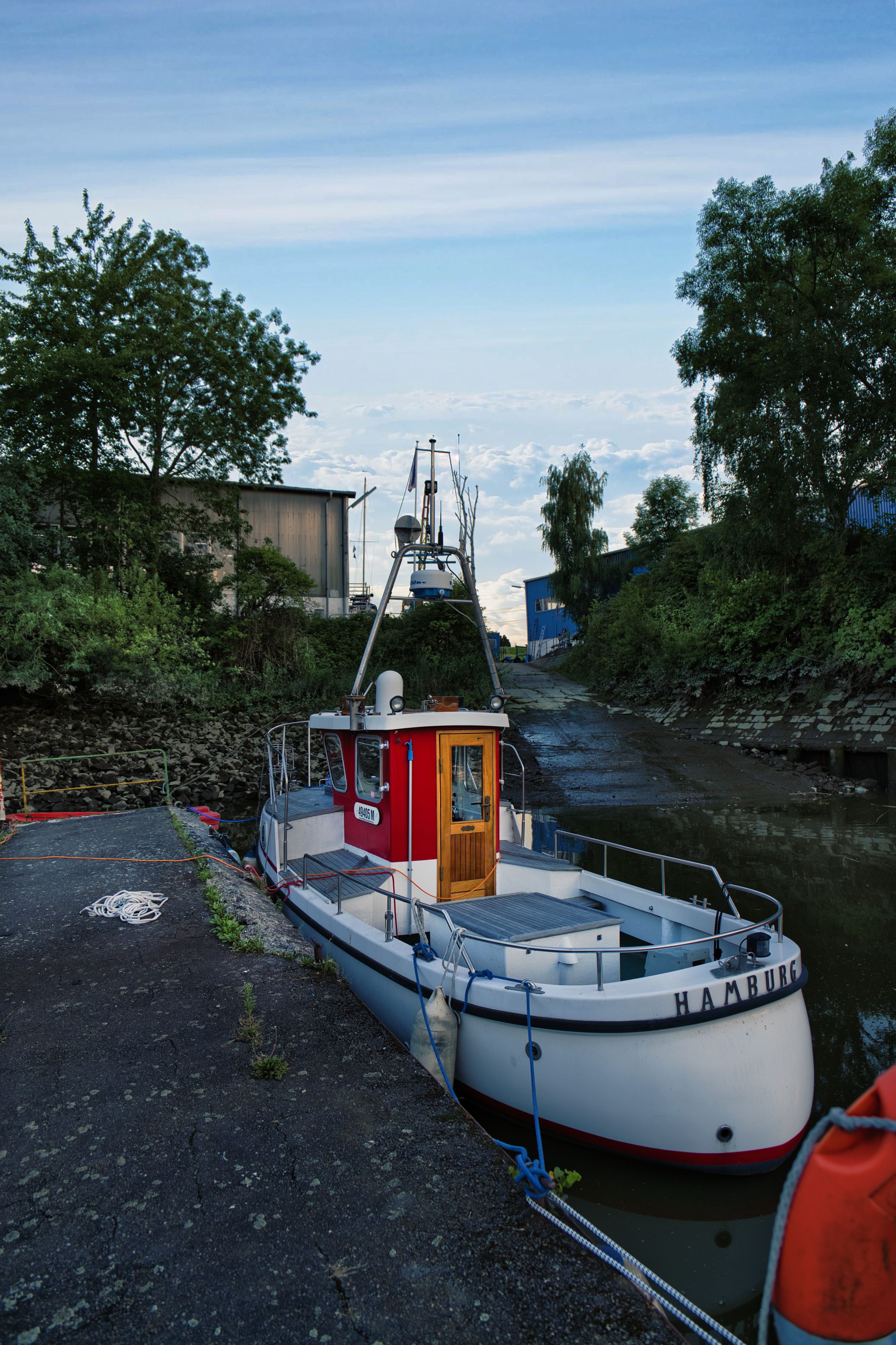 A scenic view of a boat named Hamburg docked in a tranquil canal, surrounded by lush greenery.