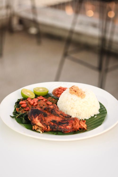 Free Delicious Indonesian dish featuring grilled chicken, rice, and fresh vegetables on a banana leaf. Stock Photo