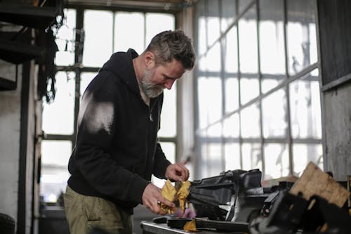 Serious adult bearded worker working with tools in workshop