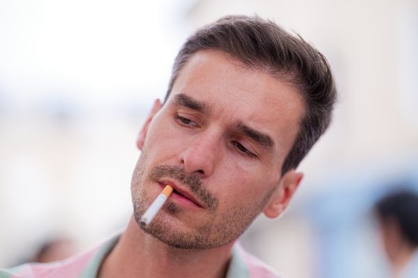 Gros plan sur un homme fumant en extérieur, expression pensive et ambiance cinématographique