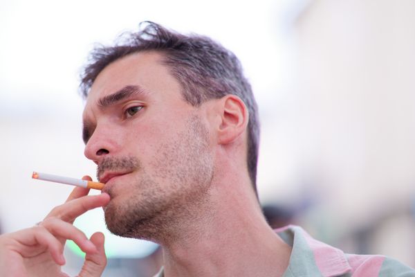 Homme décoiffé par le vent fumant de profil sous une lumière vive