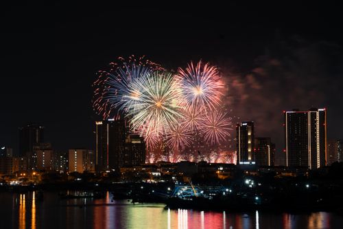 Free A vibrant display of fireworks lights up the city skyline against a clear night sky, reflecting on the water below. Stock Photo