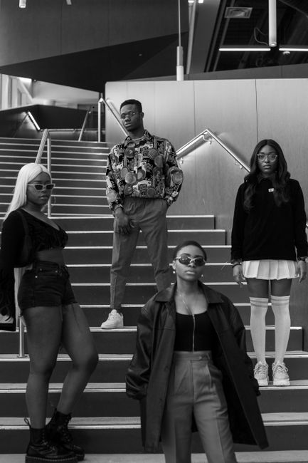 Black and white of young stylish African American teens in trendy outfits and eyeglasses standing on staircase of modern building