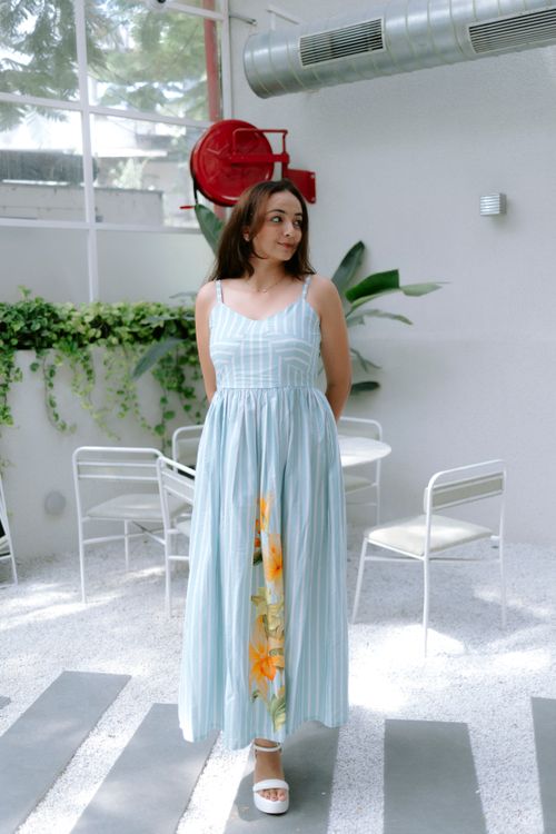 Free Woman in a light blue maxi dress with floral design, standing in a modern indoor setting. Stock Photo