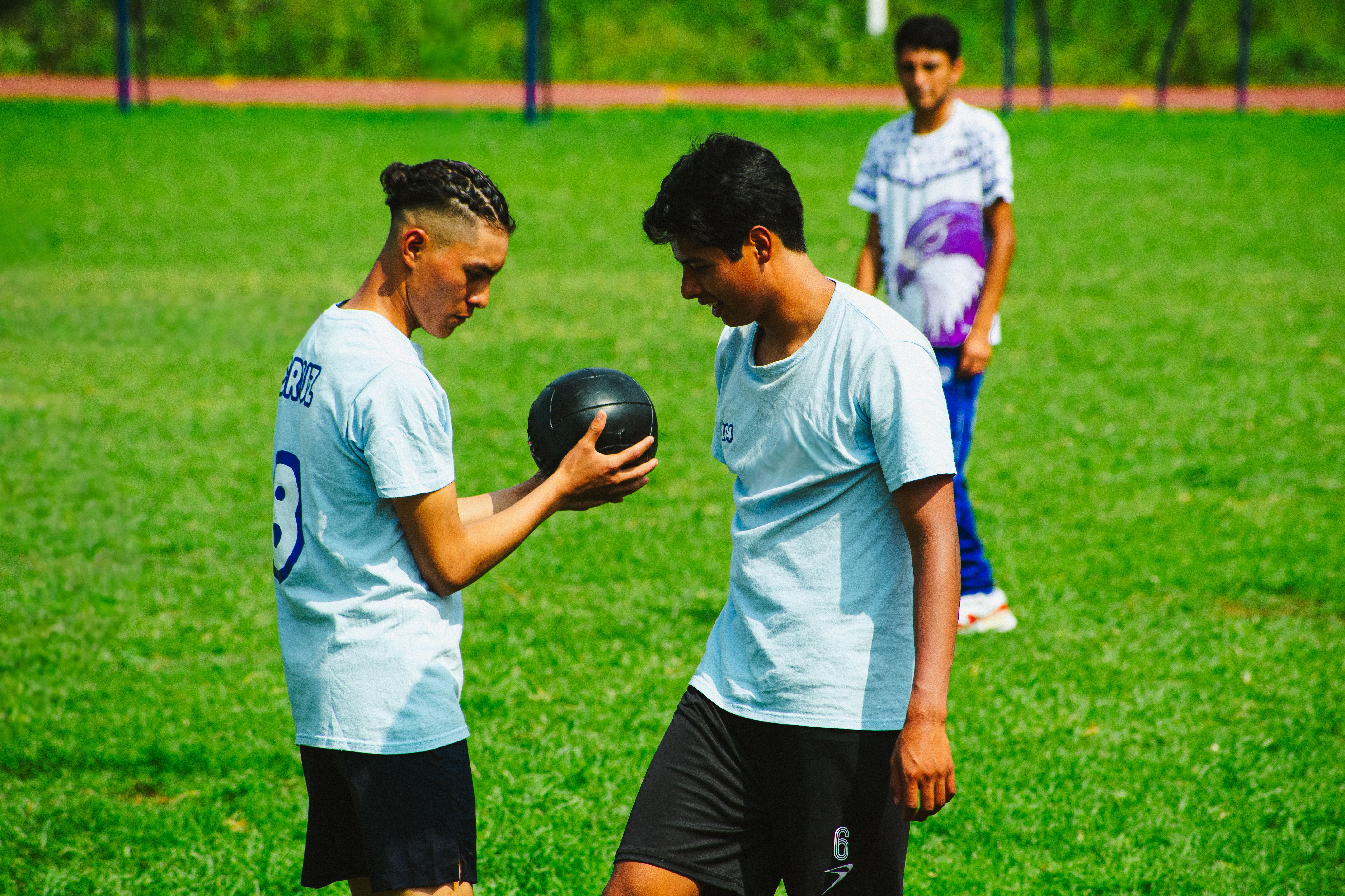 Two young athletes practicing with a medicine ball on a sports field in Mexico City.