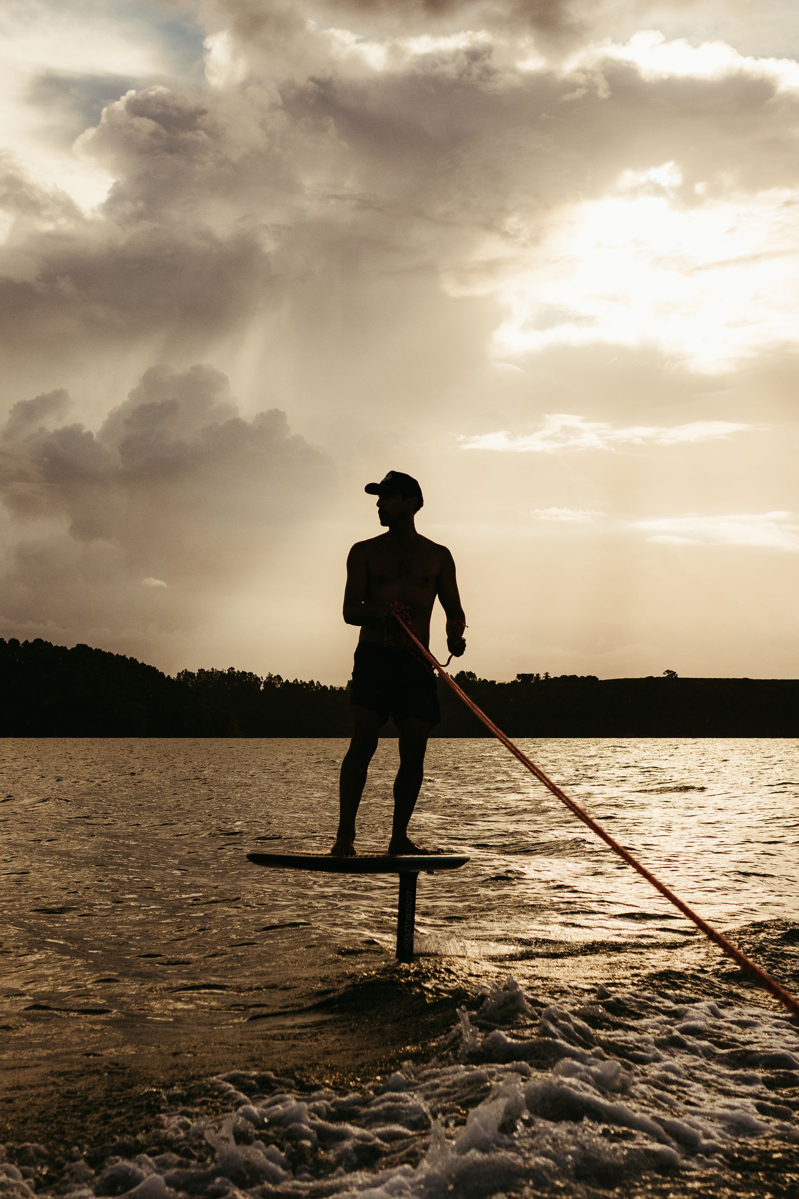 Foil surfer silhouette riding a wave at dramatic sunset
