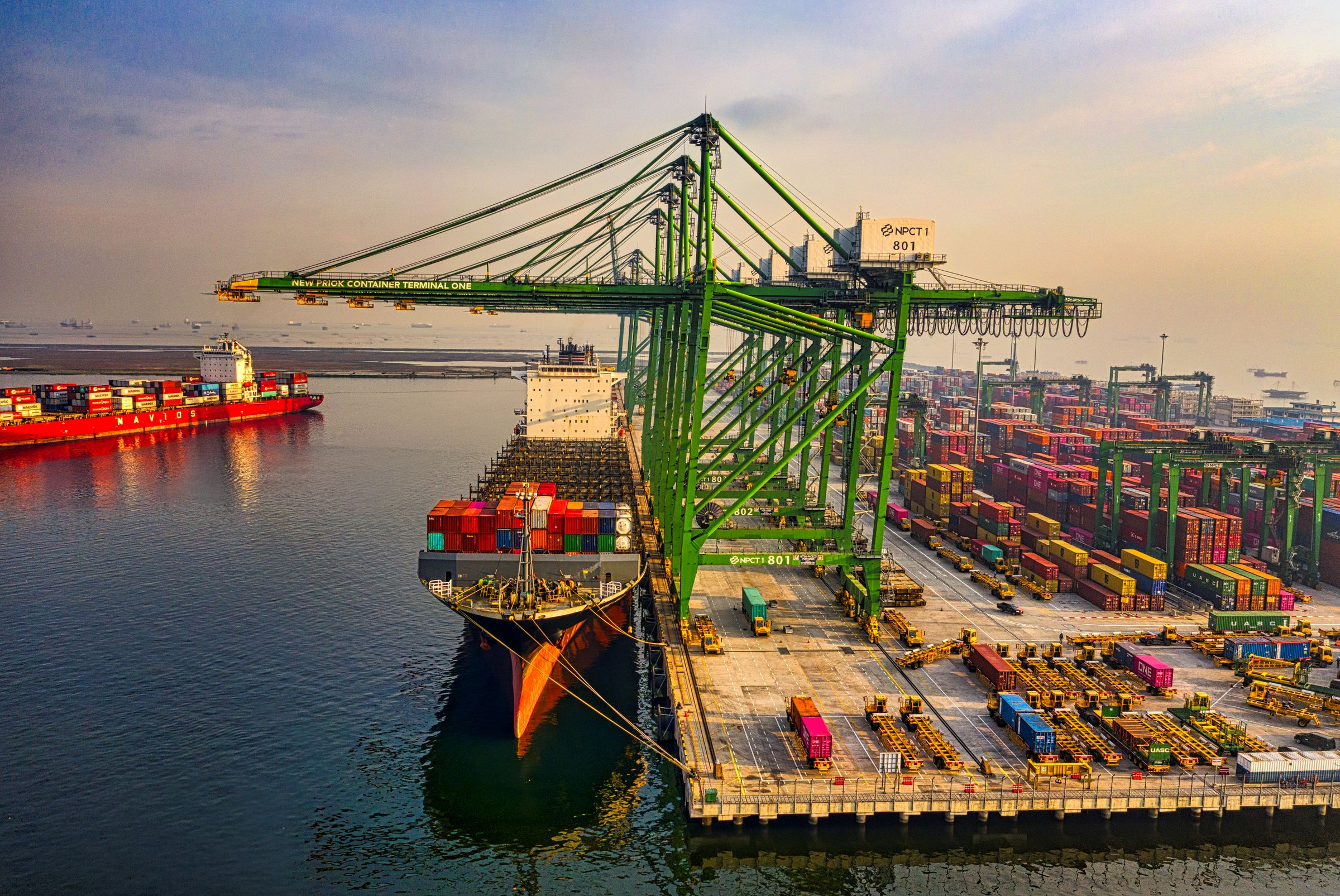 A gantry crane loading containers onto a ship at a port at first light
